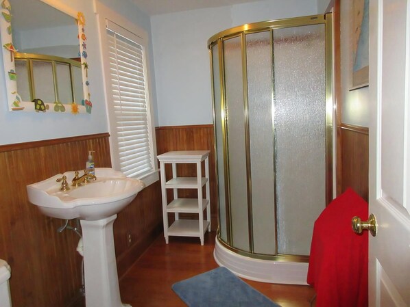 A bathroom with a white pedestal sink, a glass shower enclosure, and a small white shelf.