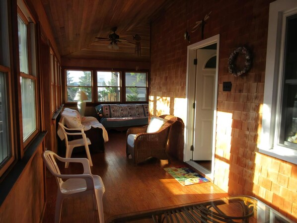 A room with a wooden ceiling, a ceiling fan, a sofa, a dining table, and a door.