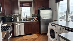 Une cuisine moderne avec des meubles en bois, un réfrigérateur en acier inoxydable, un lave-vaisselle, un lave-linge et une fenêtre donnant sur des immeubles.