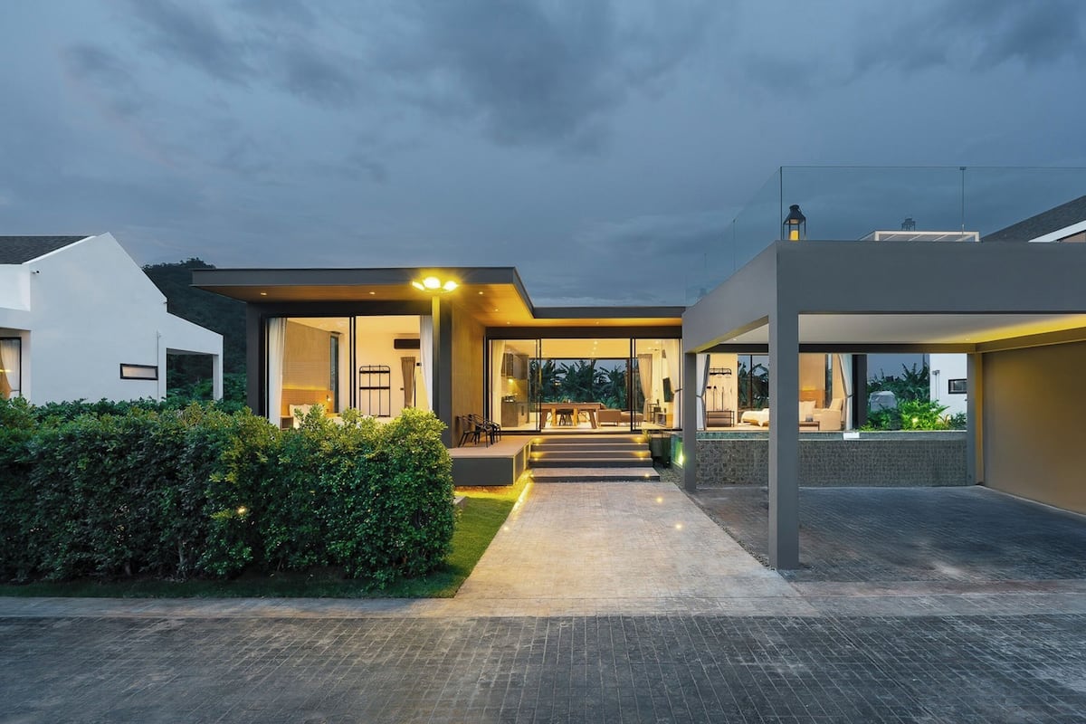 A modern house with a spacious patio, a well-lit entrance, and a view of the surrounding greenery.