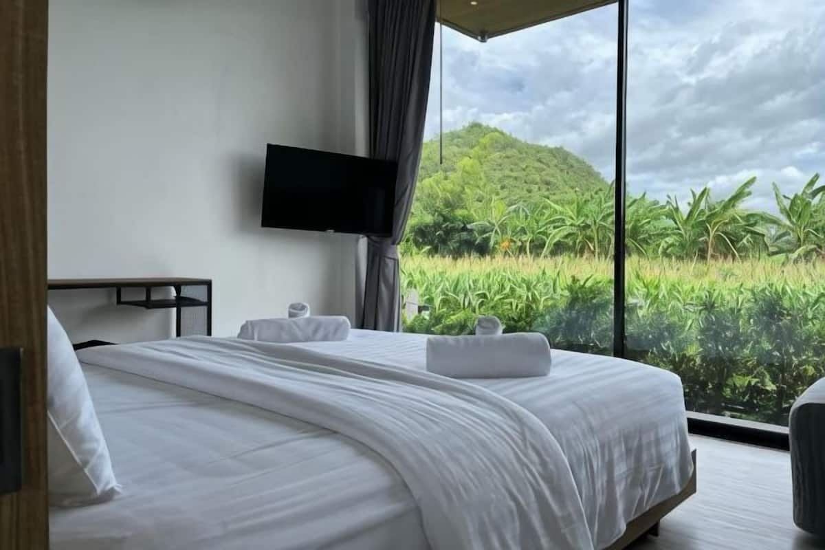 A hotel room with a large bed, a flat-screen TV, and a view of a lush green landscape.