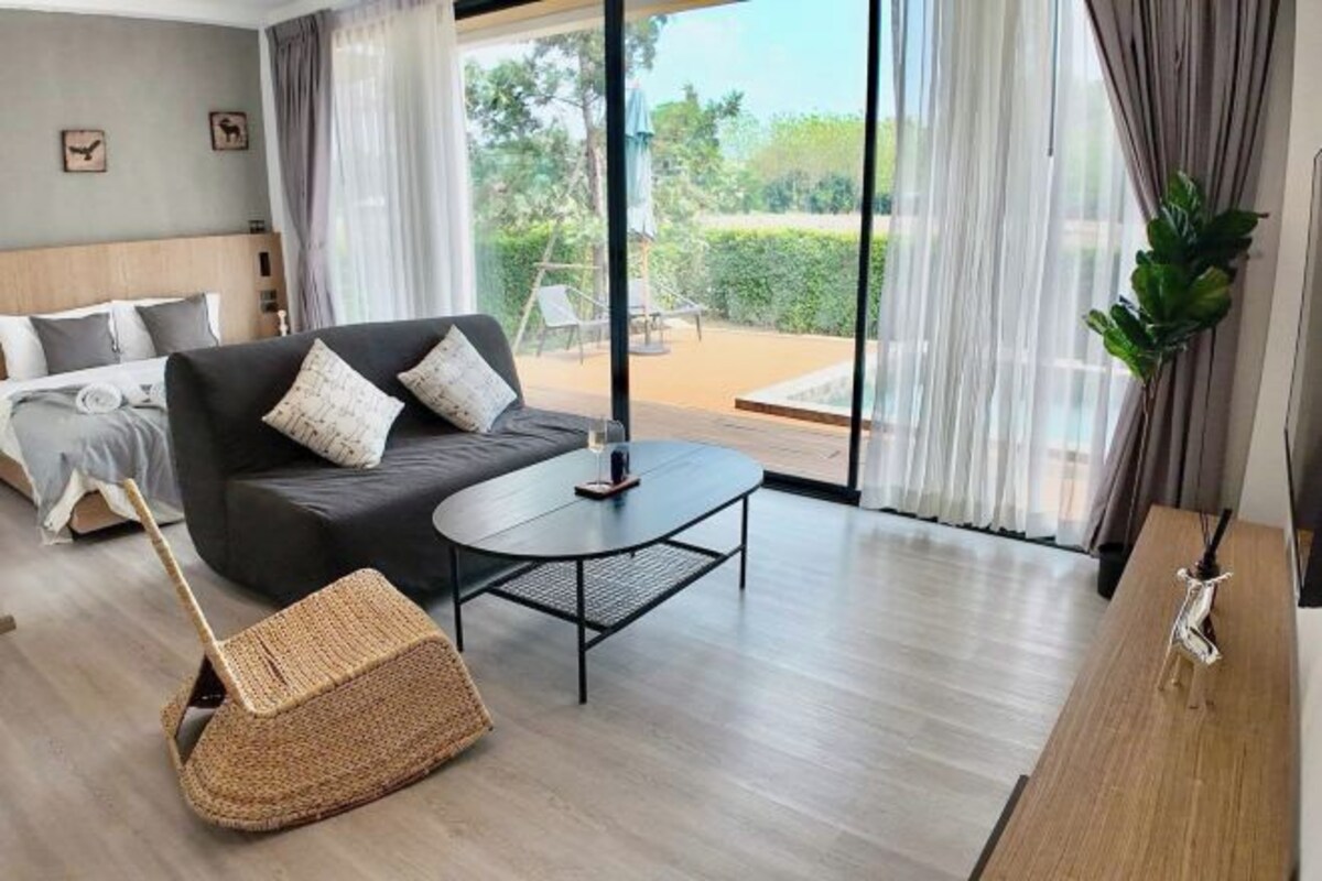 A modern hotel room with a large bed, a sofa, a coffee table, and a view of the outdoors.