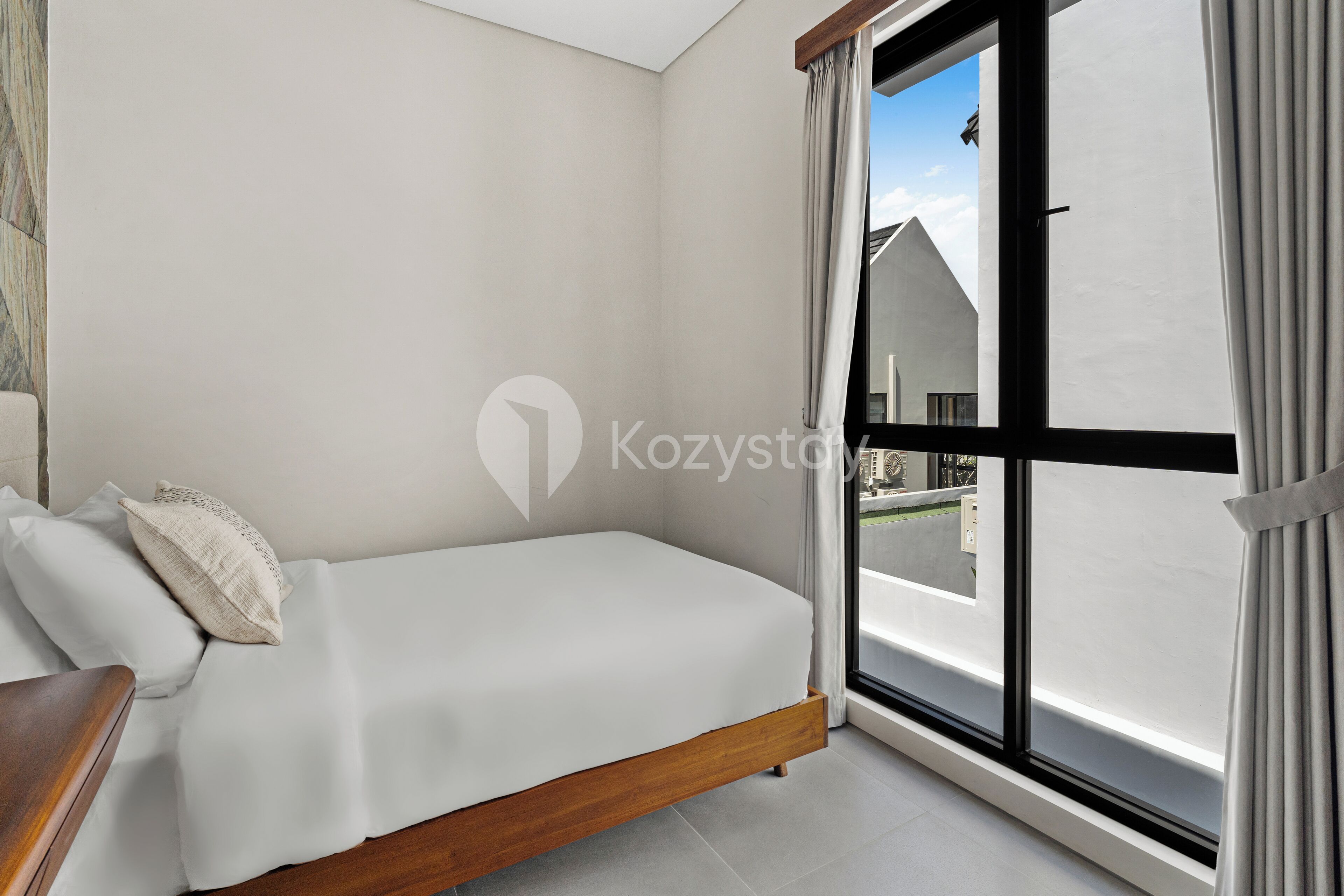 A modern bedroom with a bed, a wooden nightstand, and a large window with curtains.