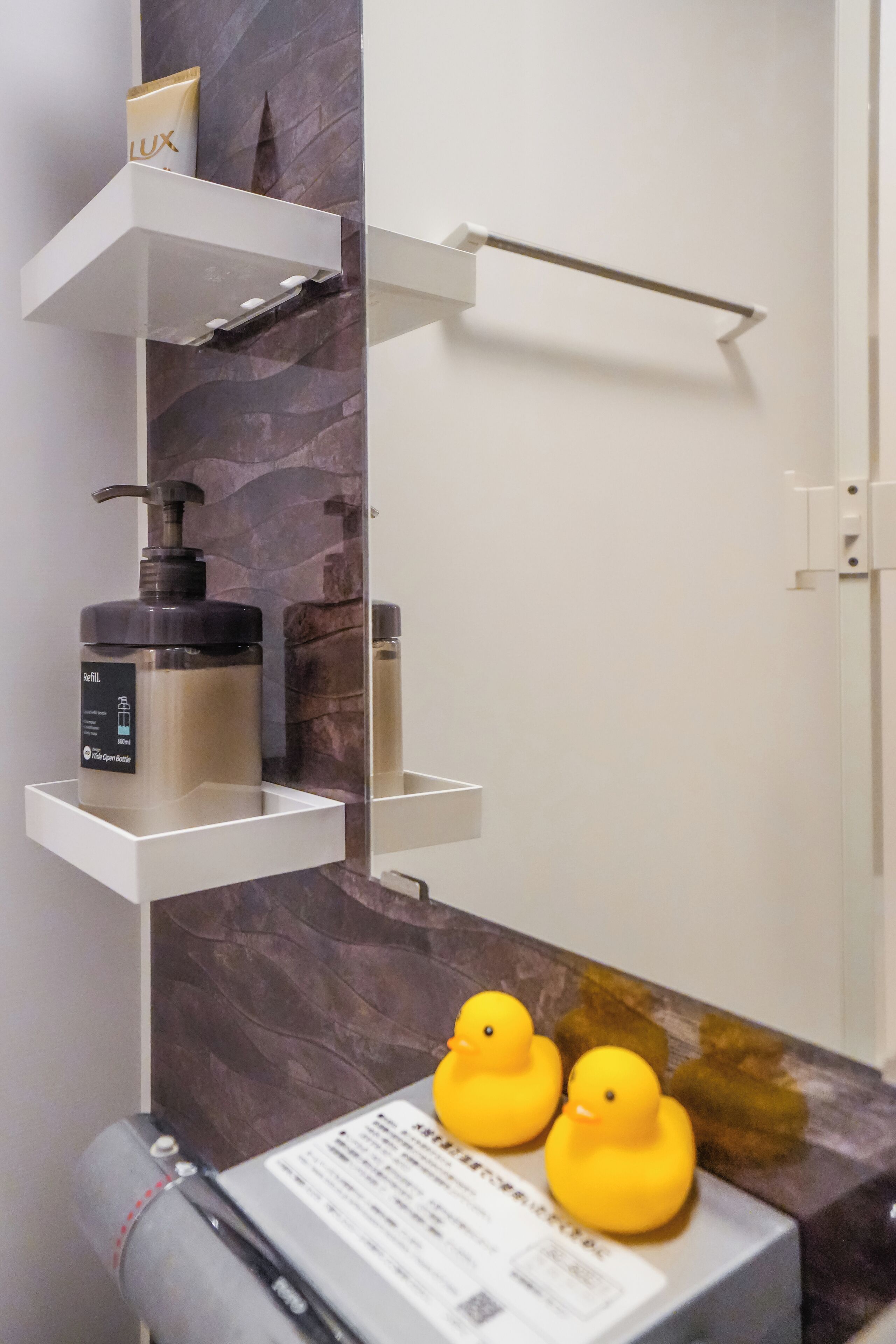 A bathroom with a marble wall, a white shelf with toiletries, and two rubber ducks on a counter.