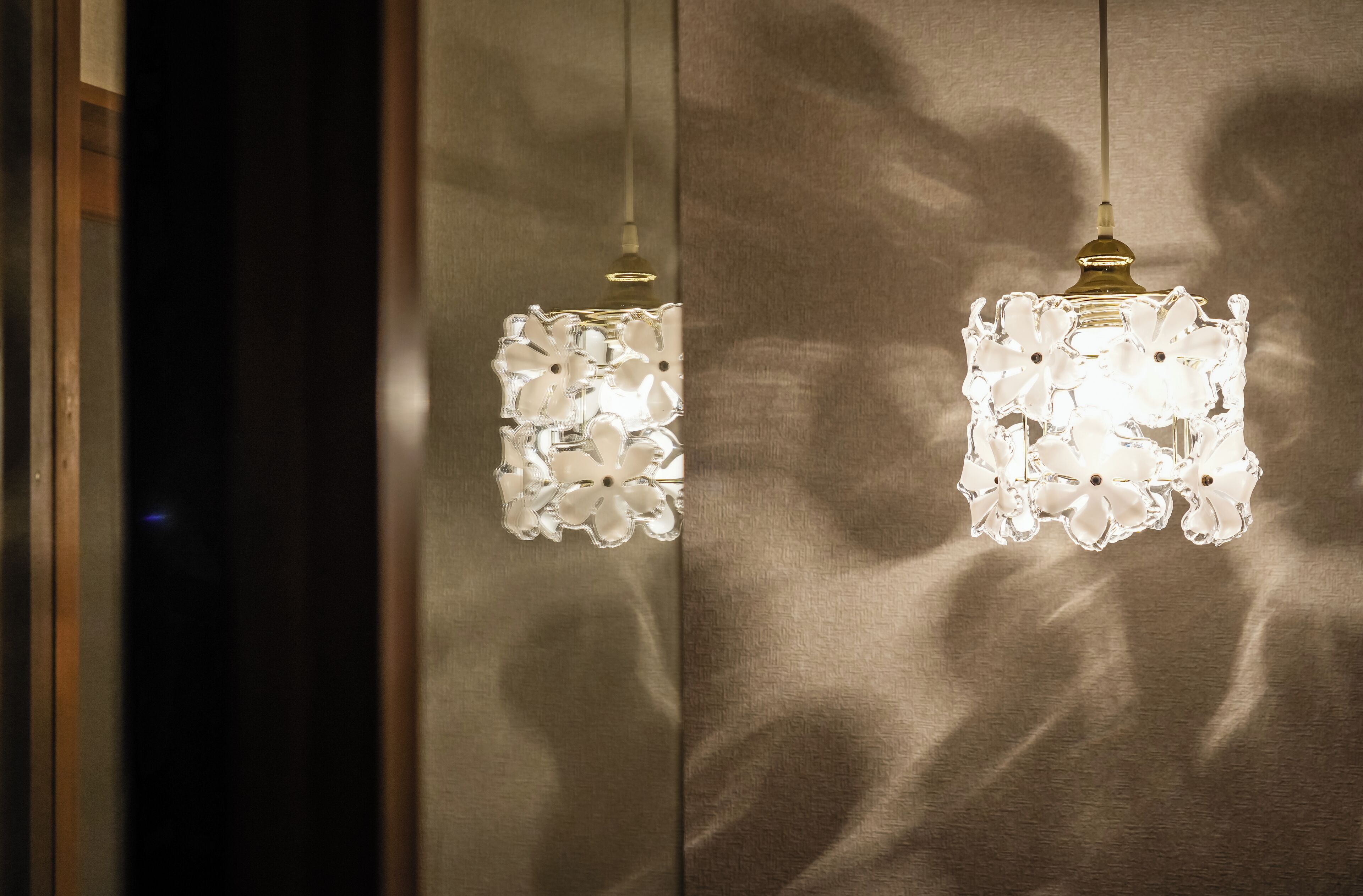 Two hanging crystal chandeliers with a floral design against a textured wall.