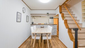 A modern kitchen with a dining area, wooden flooring, and a staircase with a wooden handrail. - HANASTAY NODA (Osaka)