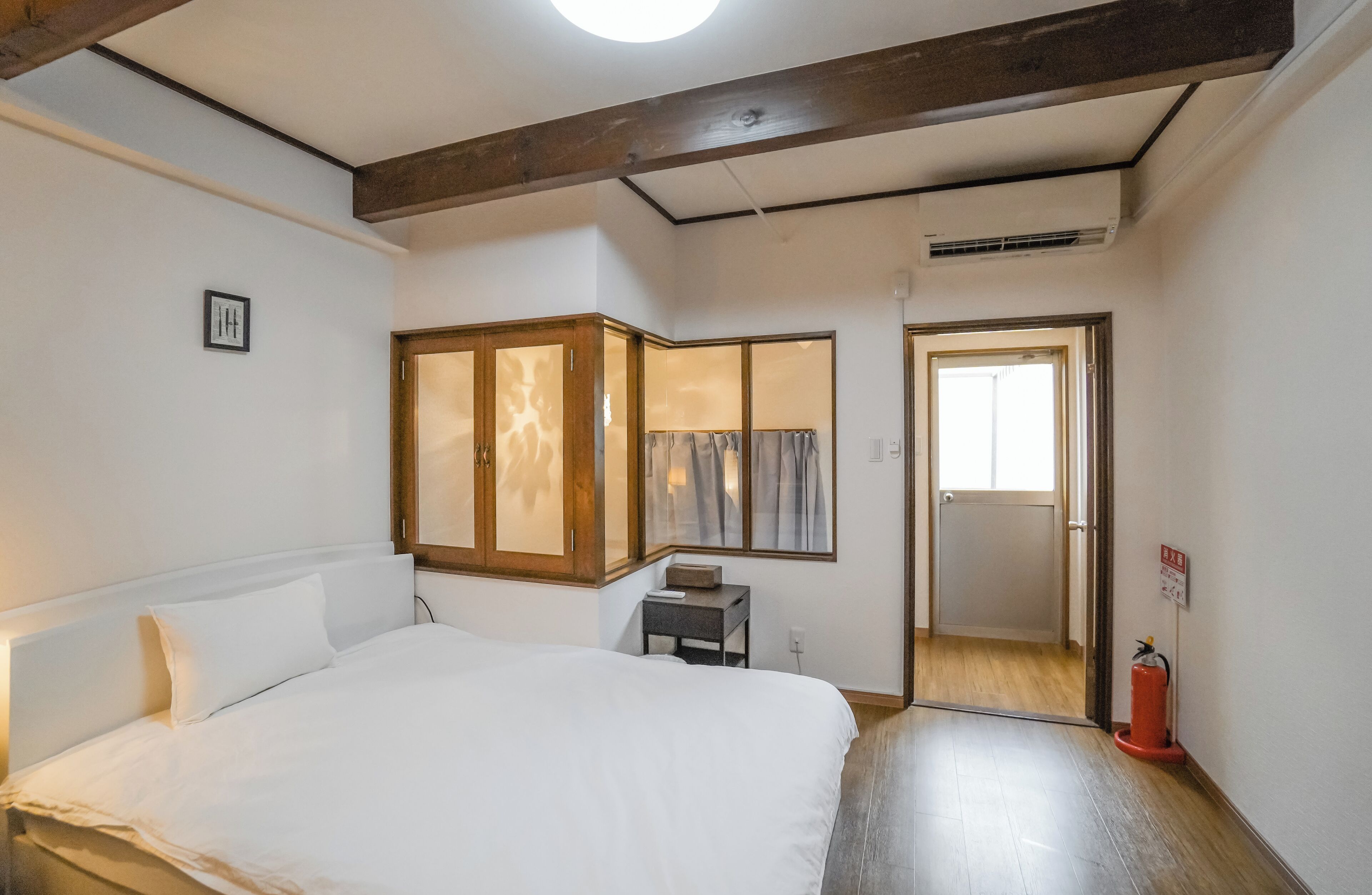 A bedroom with a bed, a small table, a wardrobe, and a door leading to another room.