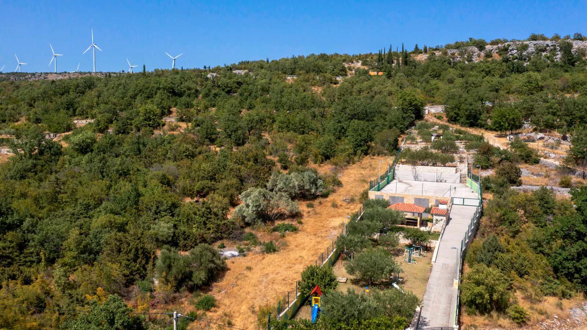 A hillside with wind turbines, a playground, and a building with a paved area.