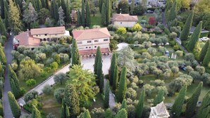 An aerial view of a residential area with a central building surrounded by well-maintained gardens and tall trees. - Villa Paradiso (Sirmione)