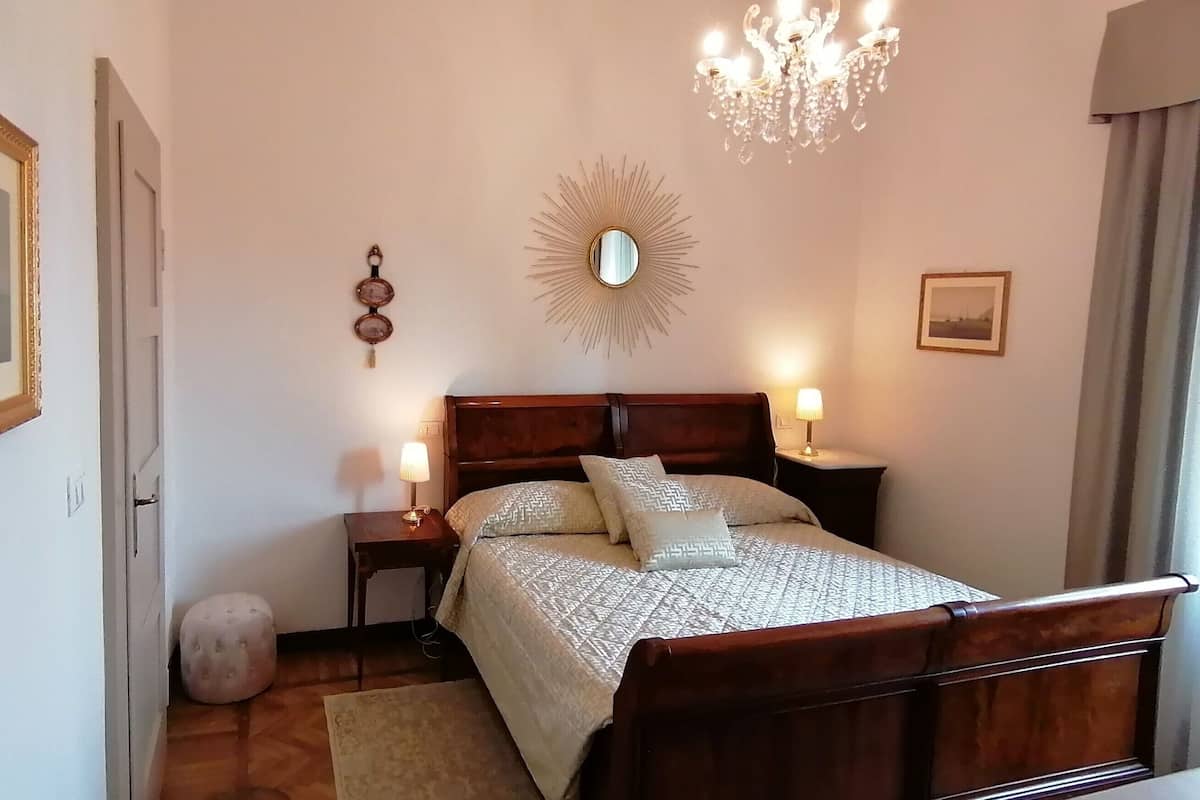 A bedroom with a wooden bed, a chandelier, a round mirror, and a bedside table with a lamp.