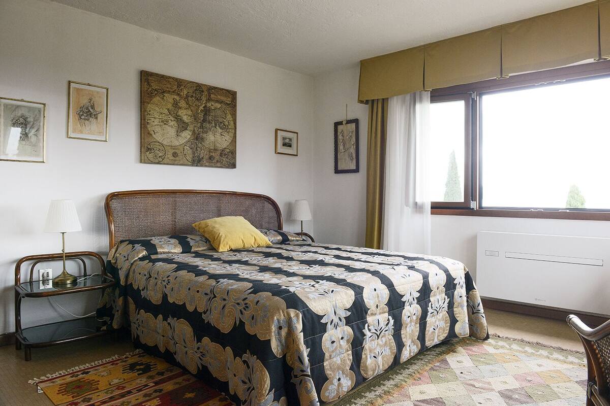 A bedroom with a large bed, two bedside tables, a window with curtains, and a map on the wall.