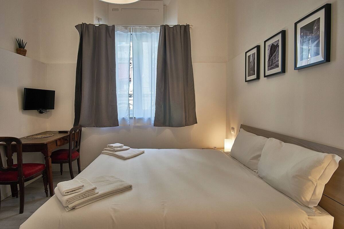 Ein Hotelzimmer mit einem Bett, einem Schreibtisch mit Stuhl, einem Fernseher und drei gerahmten Bildern an der Wand.