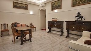 A dining area with a wooden table and chairs, a cream-colored sofa, and a dark wooden cabinet with a decorative horse sculpture. - Cuore di Bologna Suites (Bologna)