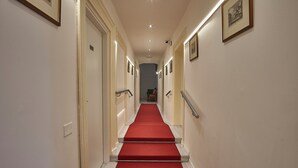 A hotel hallway with a red carpet, white walls, and framed pictures. - Cuore di Bologna Suites (Bologna)