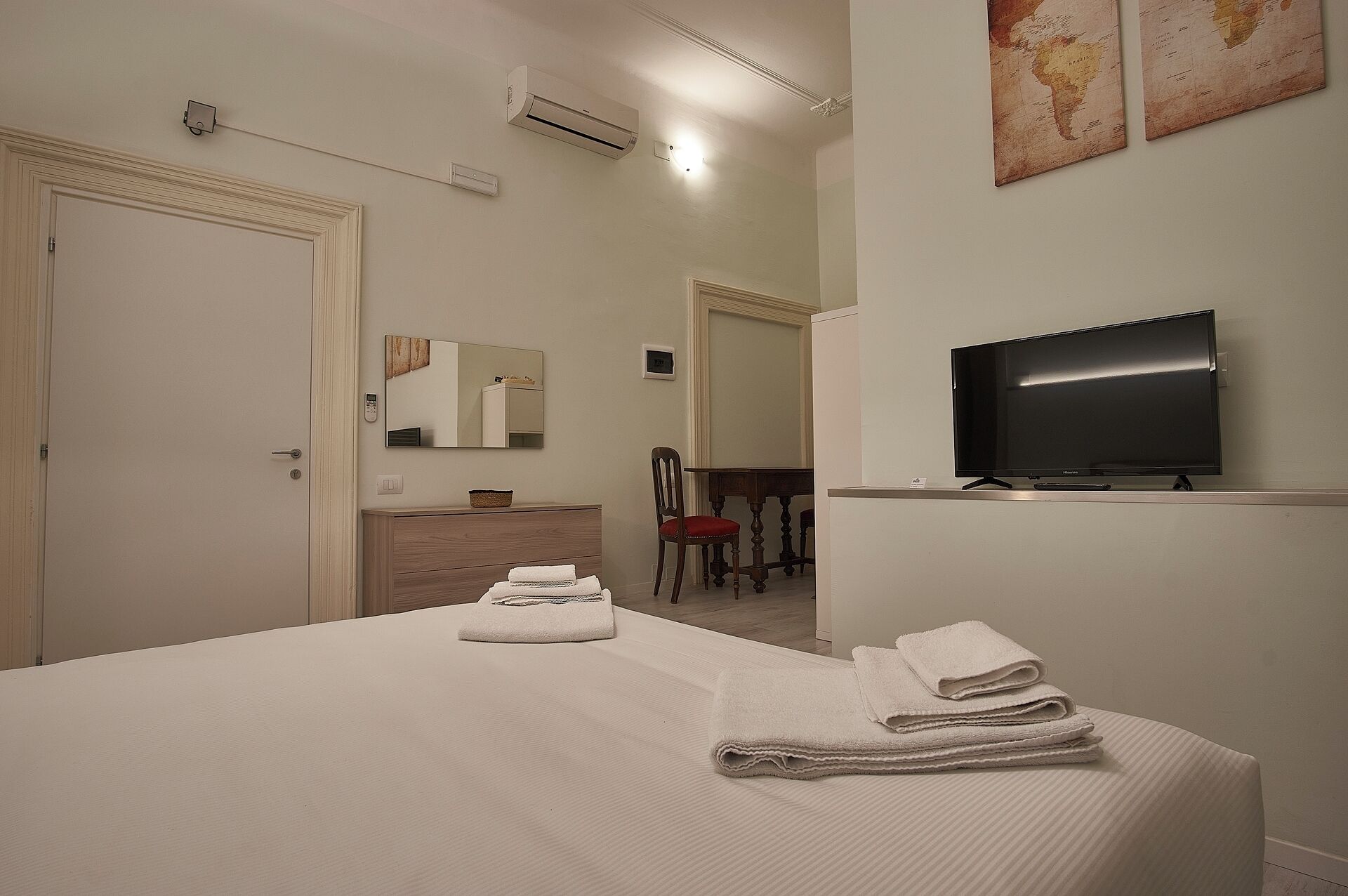 A hotel room with a bed, a television, a mirror, a chair, and a small table.