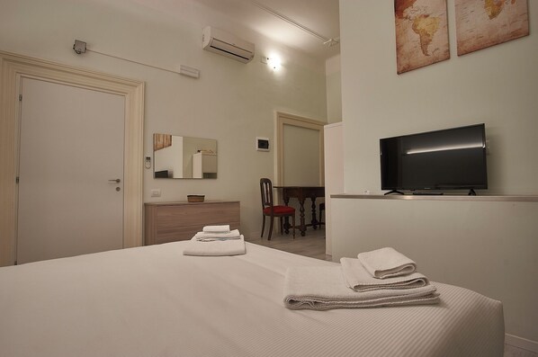 A hotel room with a bed, a television, a mirror, a chair, and a small table.
