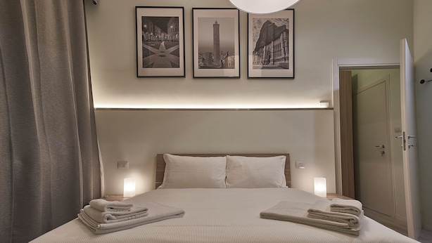A hotel room with a bed, two pillows, a nightstand, a lamp, and three framed pictures on the wall. - Cuore di Bologna Suites (Bologna)