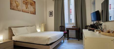 Una habitación de hotel con cama, escritorio, televisión y ventana con cortinas.