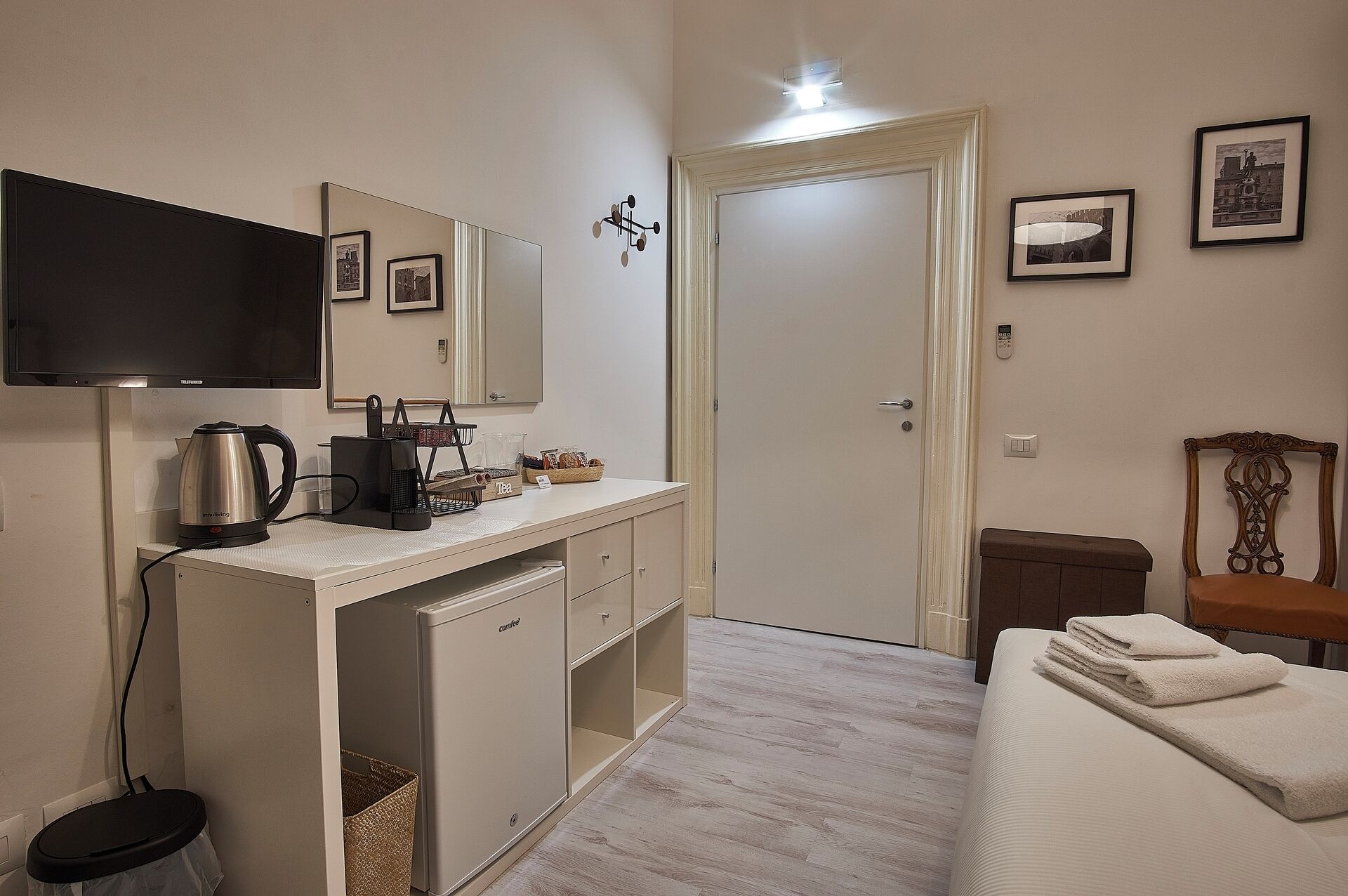 Habitación de hotel con cama, escritorio con hervidor, televisor y puerta que da a otra habitación.