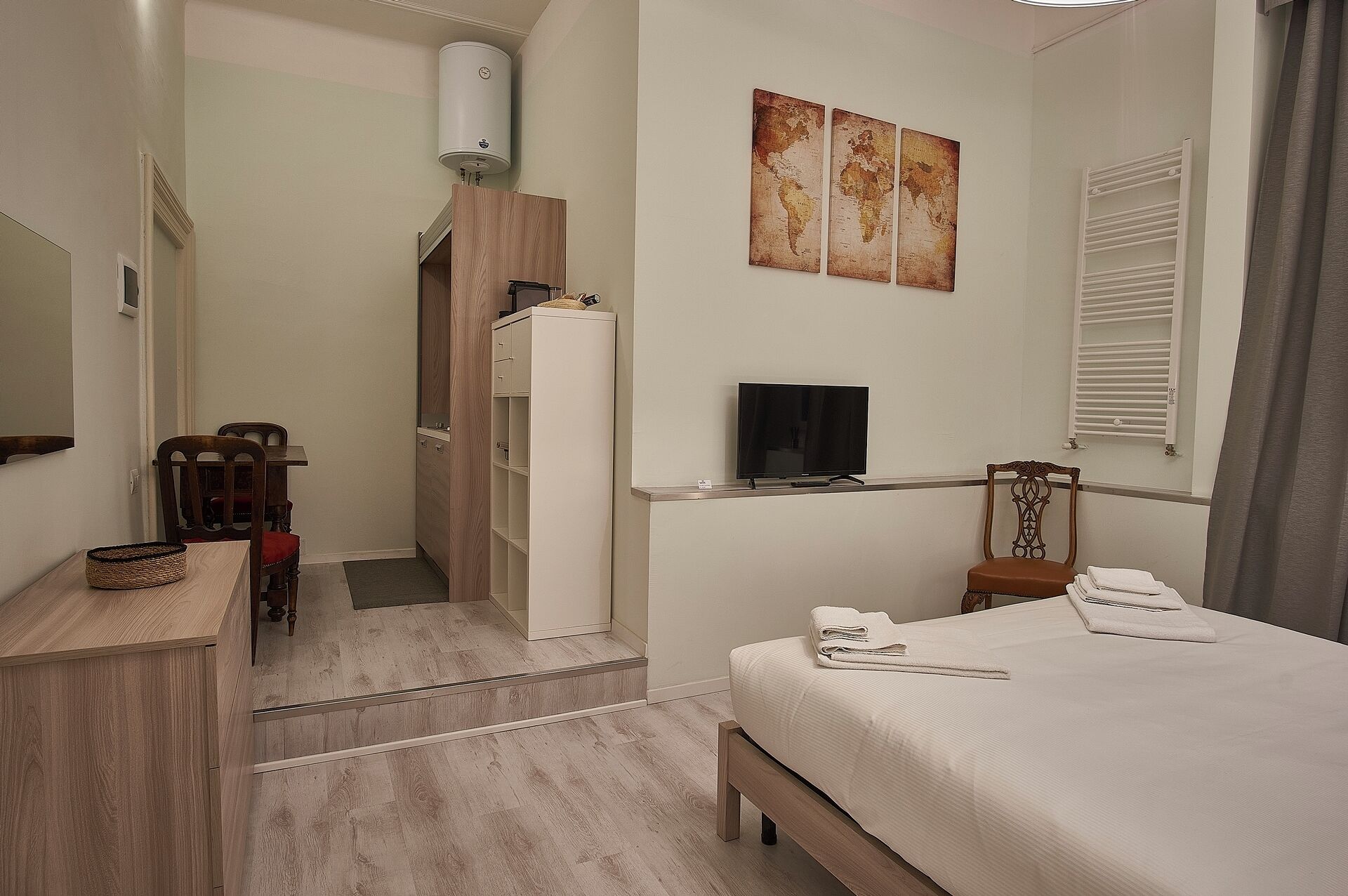 A hotel room with a bed, a TV, a desk, a chair, a wardrobe, and a radiator.