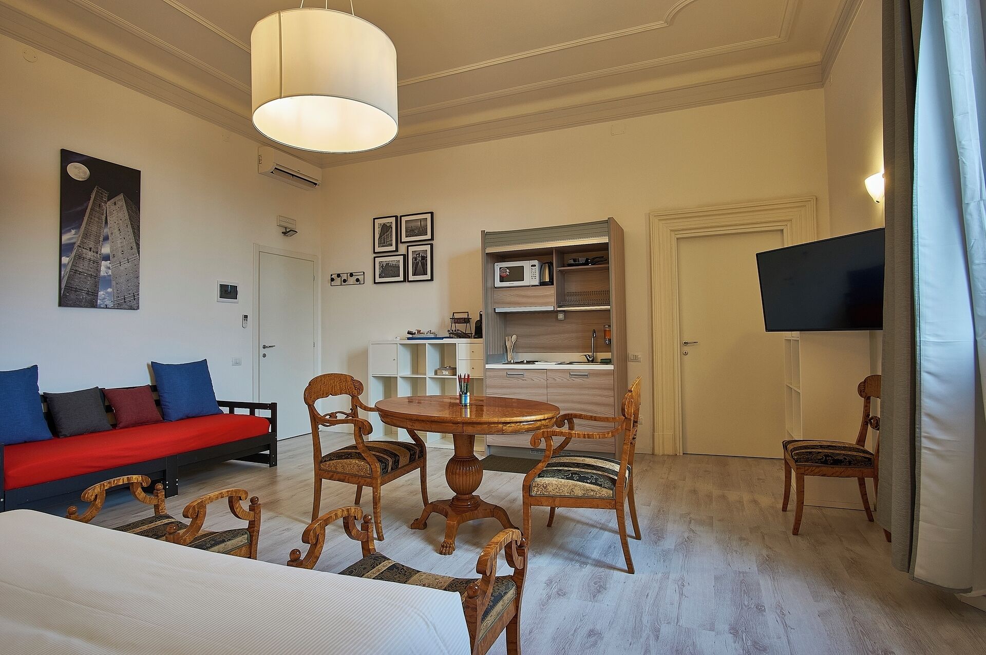 Una habitación de hotel con una cama, un sofá rojo, una mesa de comedor con sillas, una televisión y una zona de cocina.