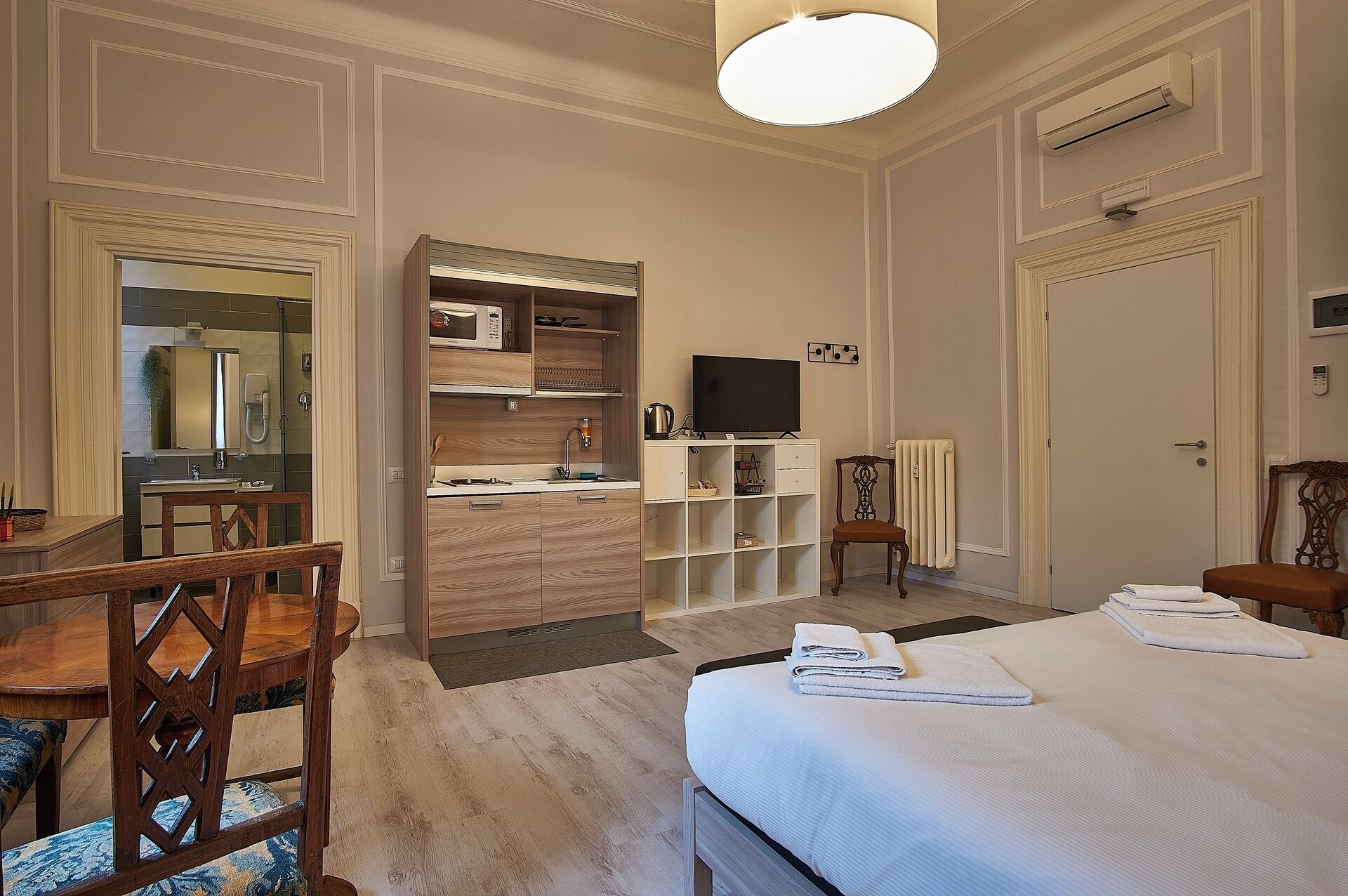 A hotel room with a bed, a TV, a desk with a chair, a microwave, a radiator, and a mirror.