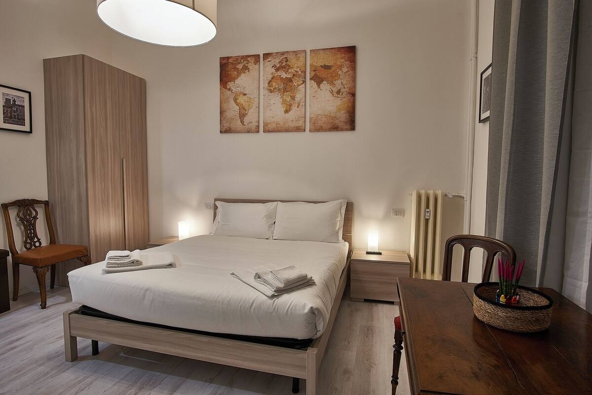Ein ordentlich eingerichtetes Schlafzimmer mit einem Bett, Nachttischen, einer Lampe, einem Sessel und einer Weltkarte an der Wand.
