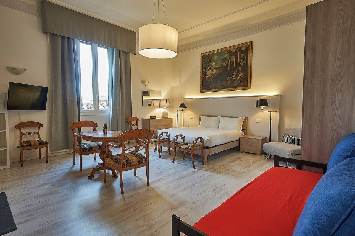 Ein Hotelzimmer mit einem Bett, Nachttischen, einem Schreibtisch mit Stuhl, einem Fernseher und einem Bild an der Wand.