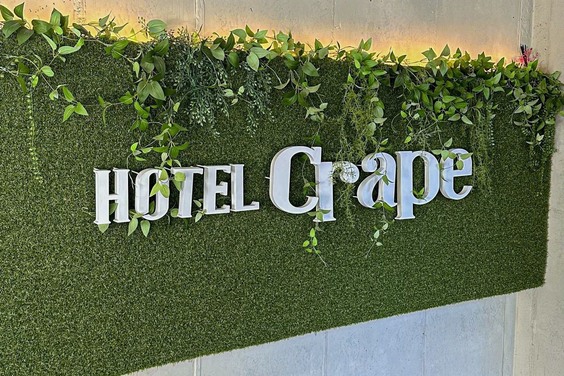 A wall with the words "HOTEL Crape" in large letters, surrounded by green foliage.