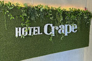A wall with the words "HOTEL Crape" in large letters, surrounded by green foliage.