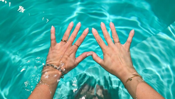 Manos sumergiéndose en agua azul cristalina.