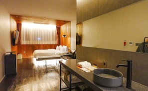 A hotel room with a bed, a desk with a sink, and a large mirror.