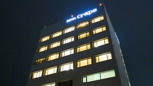 Un edificio de hotel de varios pisos con ventanas iluminadas y un letrero que dice "HOTEL CRAPE" en la parte superior.