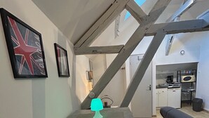 Un coin repas avec une table, des chaises et une lampe de table au néon. On aperçoit une cuisine au fond.