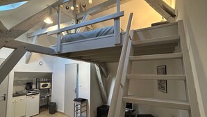 Une chambre compacte, aménagée dans un style industriel, avec un lit superposé, un bureau et un coin cuisine.