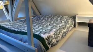 Une chambre avec un plafond en pente, un lit recouvert d’une couvre-lit à motifs, une table de chevet et un luminaire suspendu.