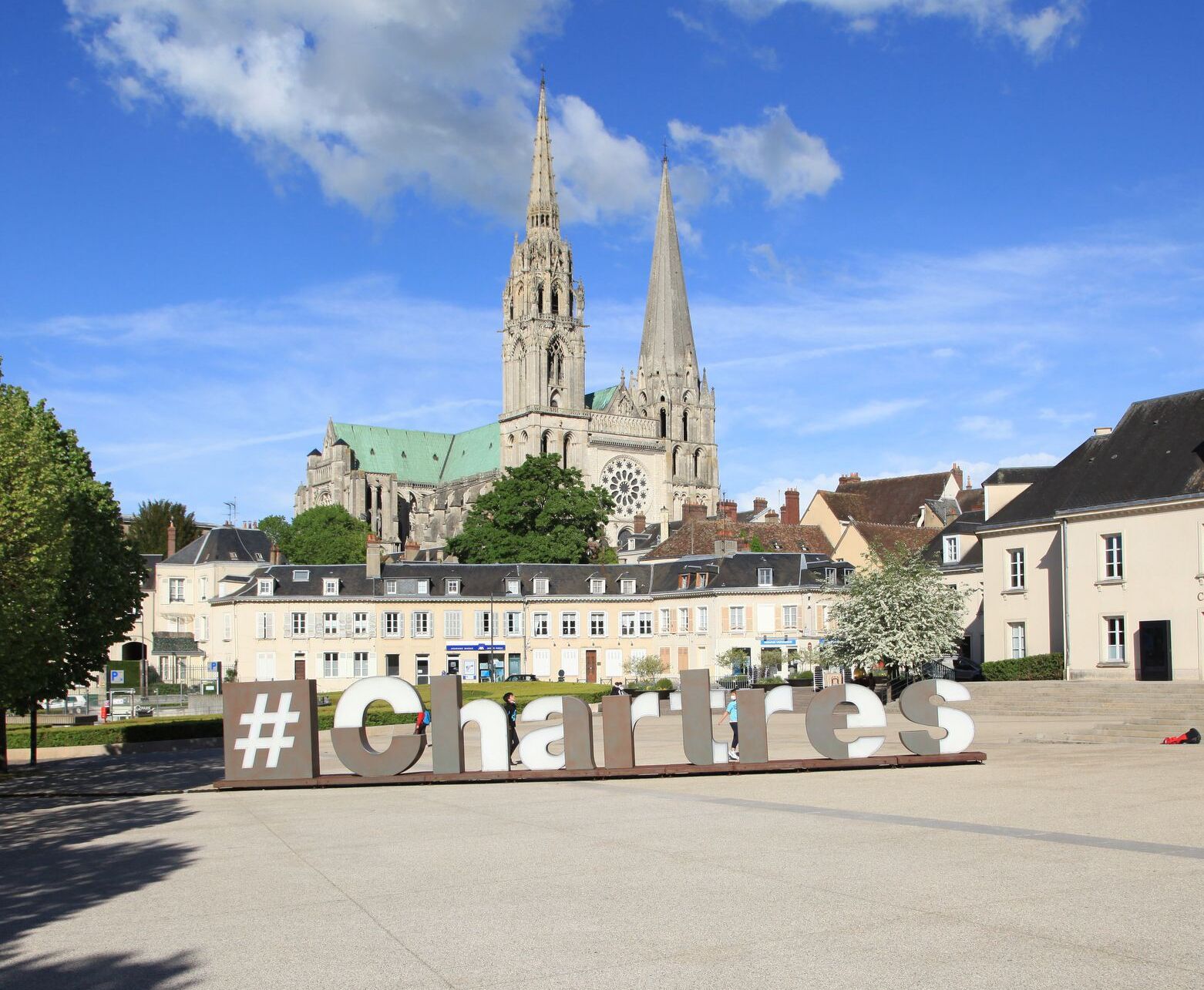 A historic cathedral with twin spires, a large sign reading "Charles," and surrounding buildings.