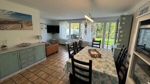 A dining area with a table set for six, a television, and a view of the garden through large windows. - Detached vacation home near Grevelingenmeer (Brouwershaven)