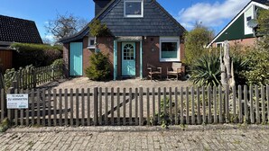 A small house with a dark roof, a green door, and a small window. There is a wooden fence in front of the house. - Detached vacation home near Grevelingenmeer (Brouwershaven)