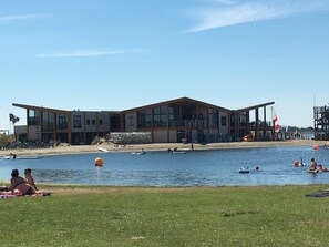 Un bâtiment moderne doté de grandes fenêtres et d’un toit plat, situé au bord d’un plan d’eau.
