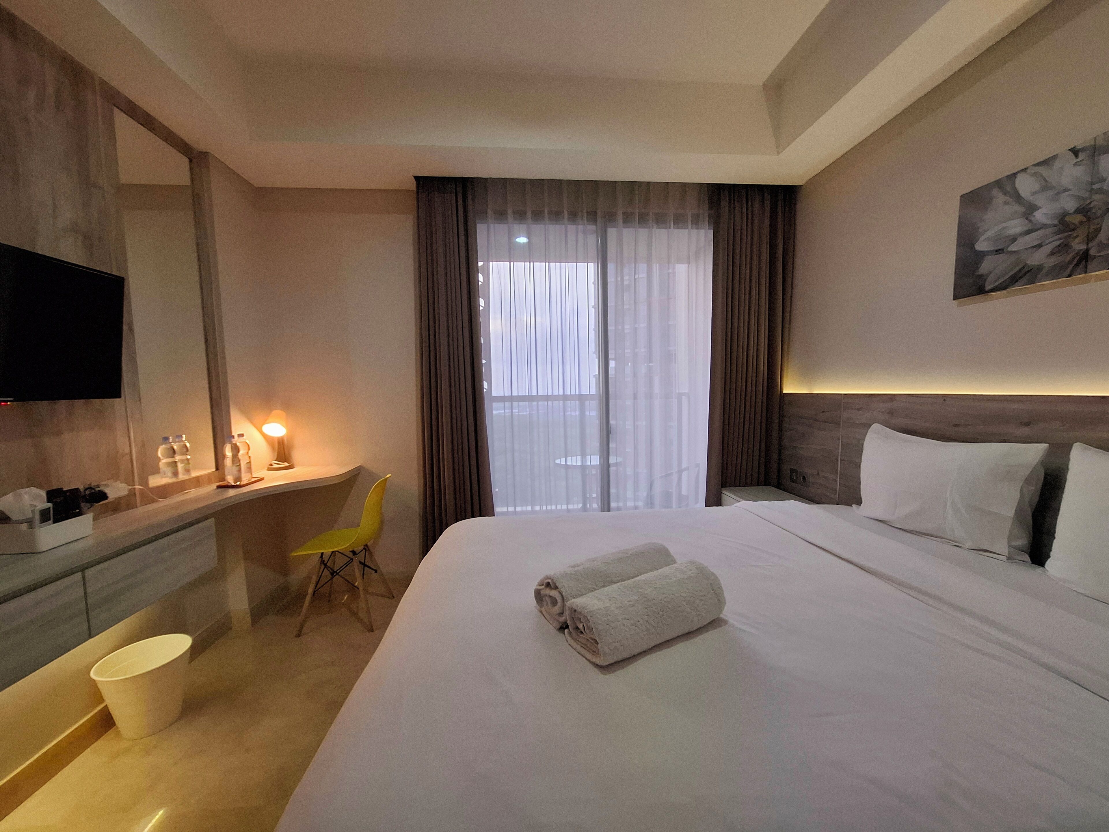 A hotel room with a bed, a desk, a chair, a TV, and a window with curtains.