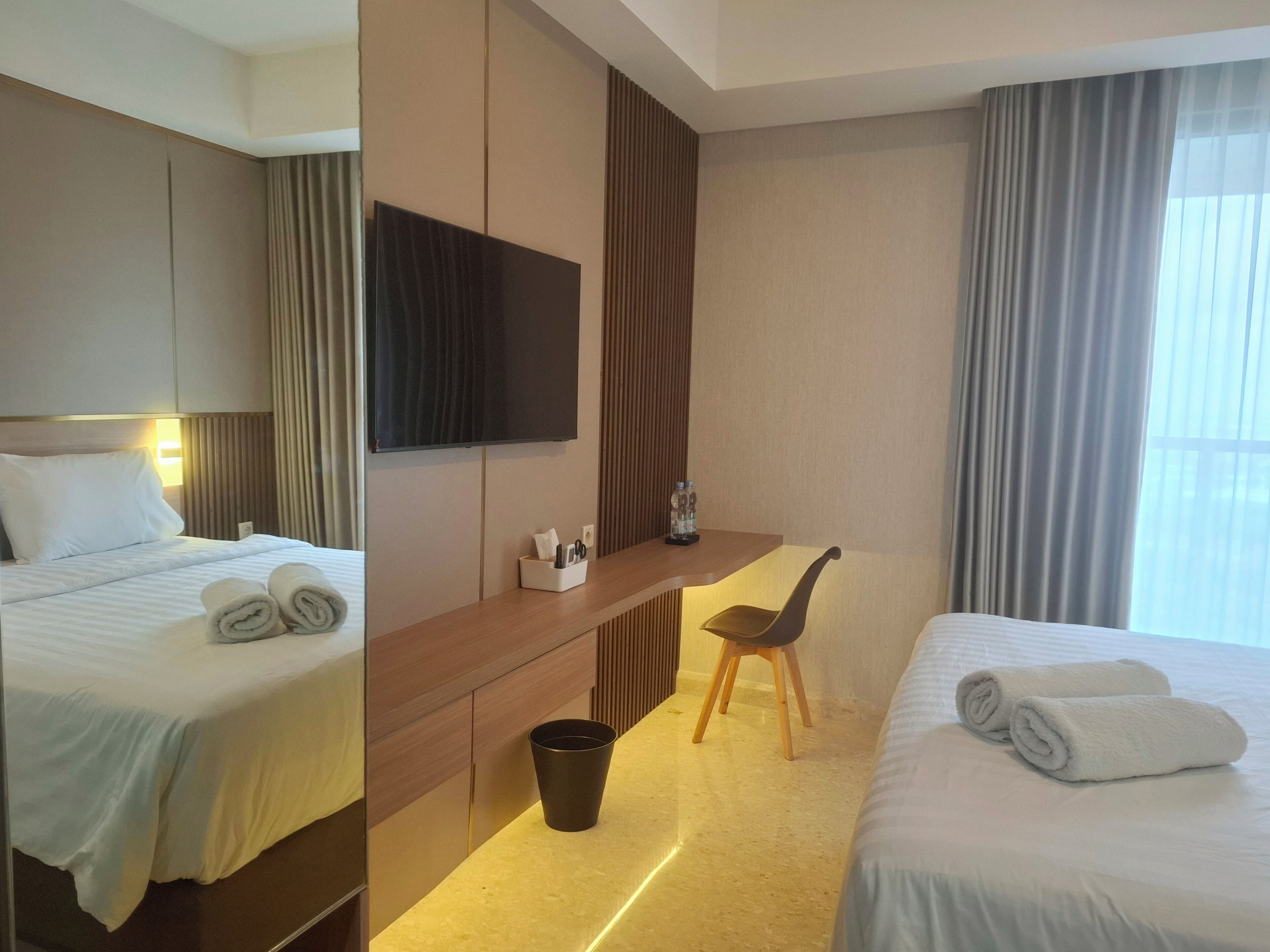 Habitación de hotel con cama, escritorio con silla, televisión y ventana con cortinas.