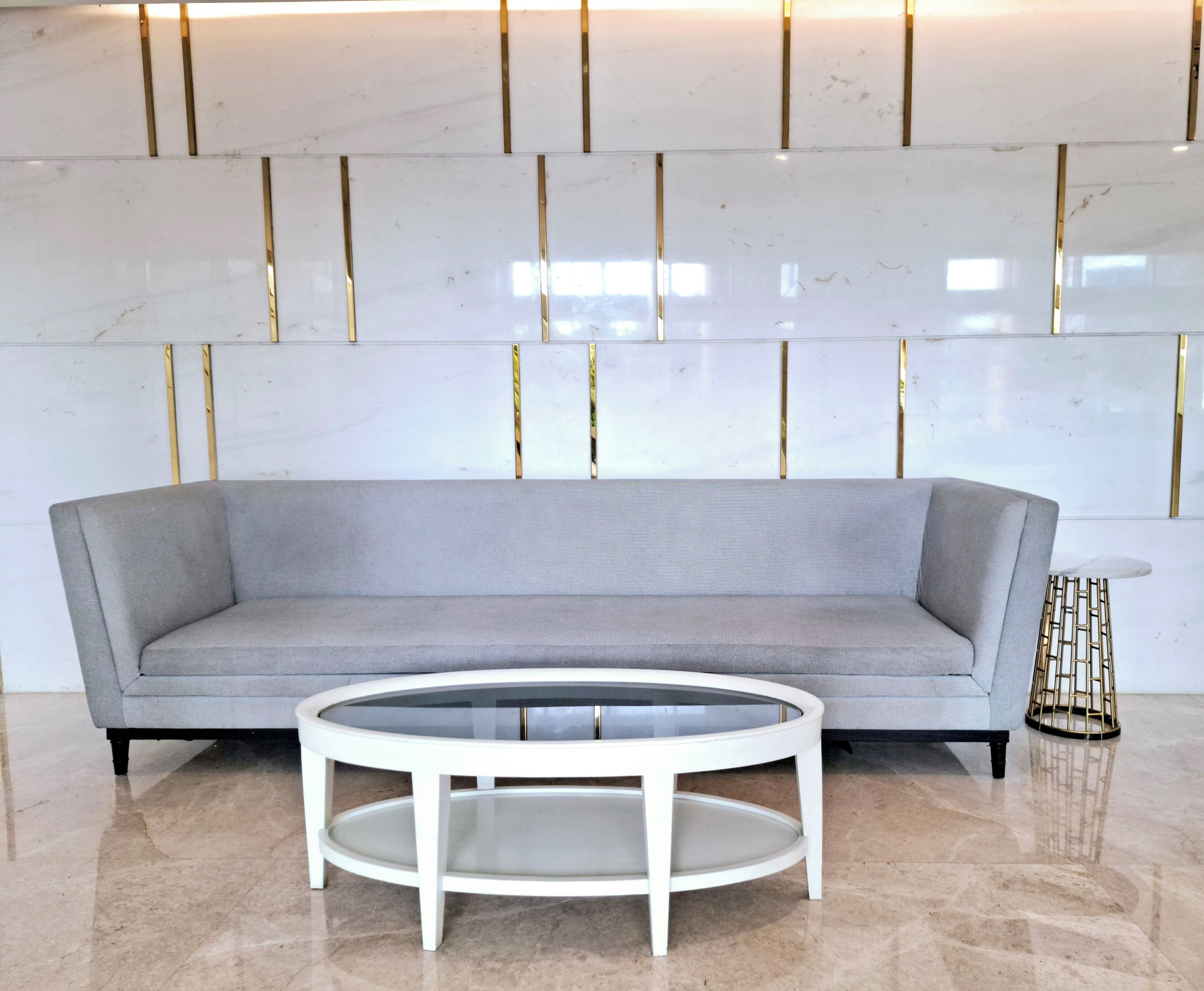 A modern living room with a grey sofa, a round glass coffee table, and a gold-framed side table.