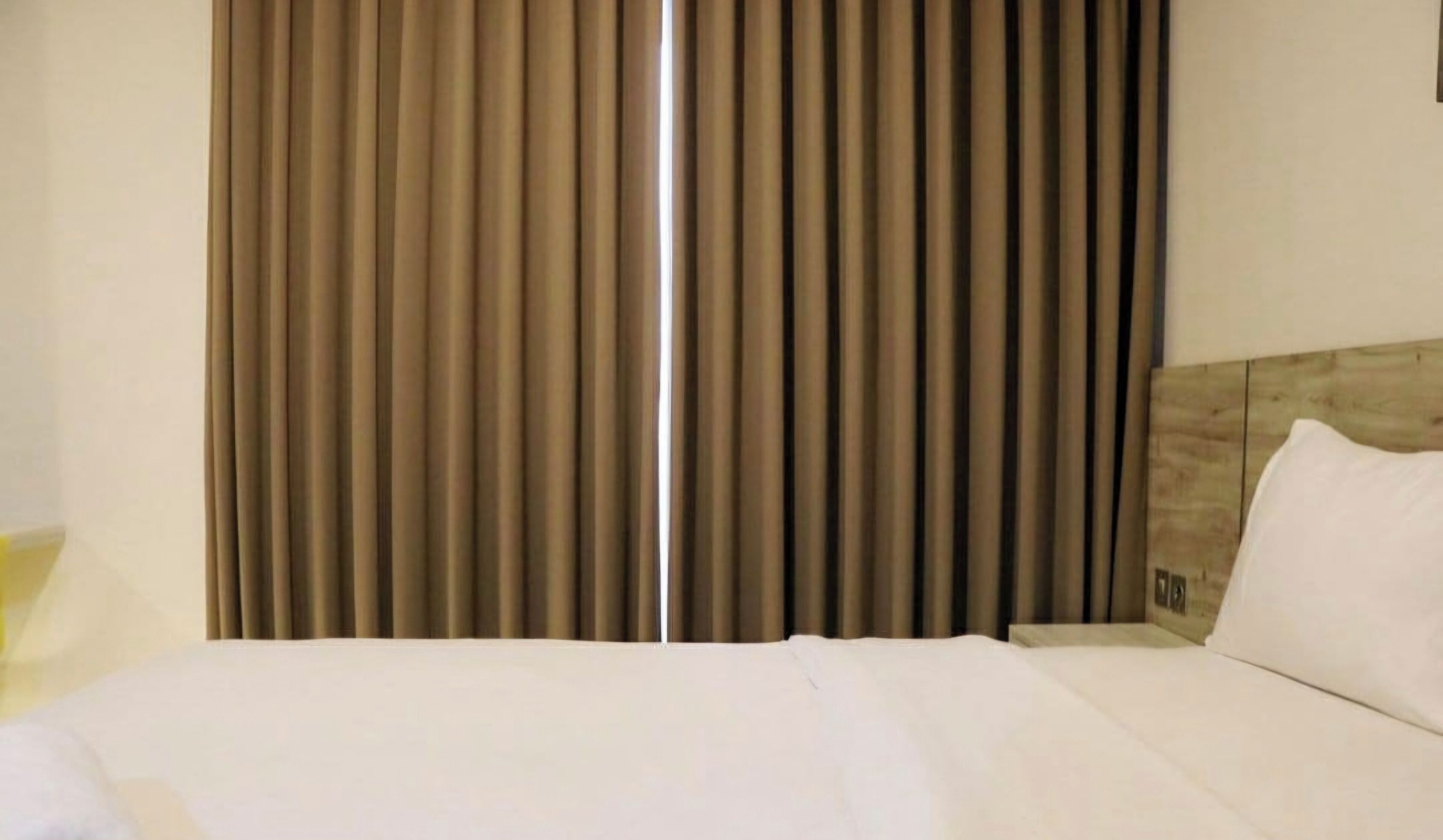 A hotel room with a bed, a headboard, and a window with vertical blinds.