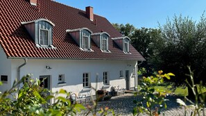 A white building with a red-tiled roof, multiple windows, and a stone-paved courtyard.