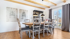 A dining area with a wooden table and chairs, pendant lights, and artwork on the walls. - Holiday Home 'Hof Vilmnitz 22 B' with Private Terrace, Private Garden and Wi-Fi (Putbus)