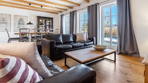 A living room with a black leather sofa, a wooden coffee table, and a dining area with chairs and a cabinet. - Holiday Home 'Hof Vilmnitz 22 B' with Private Terrace, Private Garden and Wi-Fi (Putbus)