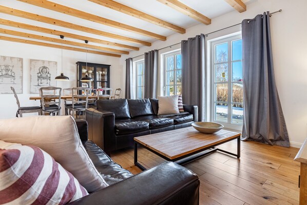 A living room with a black leather sofa, a wooden coffee table, and a dining area with chairs and a cabinet.