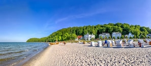 A beach with beach huts, a wooden boat, and houses on a hillside.