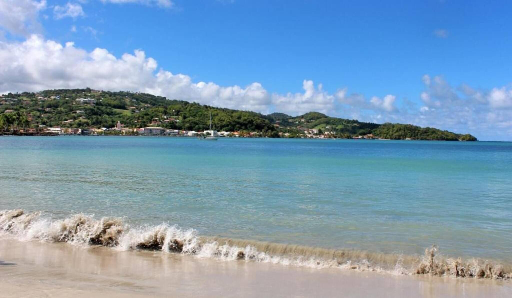 A beach with clear water and a distant view of a hilly area with buildings.